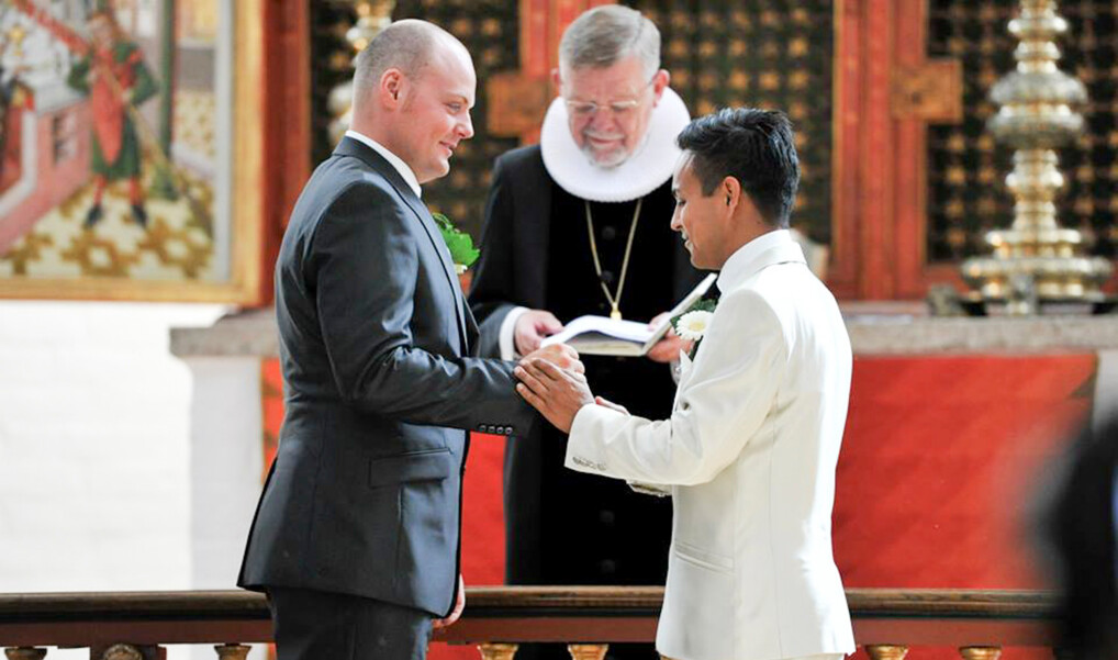 To mænd iklædt jakkesæt giver hinanden ringe på foran alteret, hvor biskop Kjeld Holm er ved at vie dem